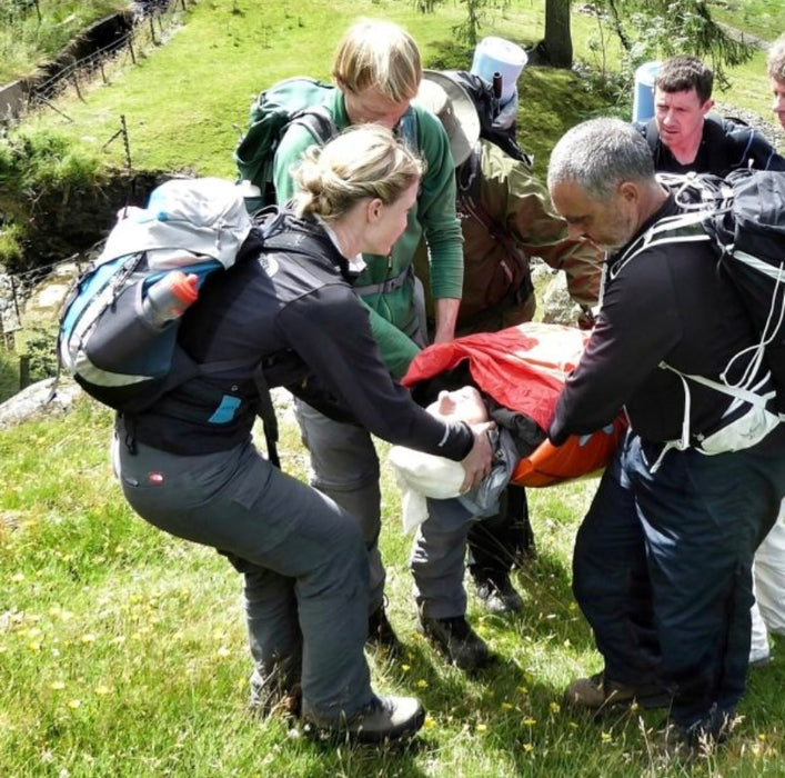 Group of people assisting a person on a stretcher in a grassy outdoor setting