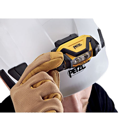 Person wearing a white hard hat with a Petzl Pixa R headlamp, held by a gloved hand.