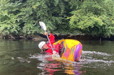 Person in a colorful kayak with a paddle, surrounded by greenery on a river.
