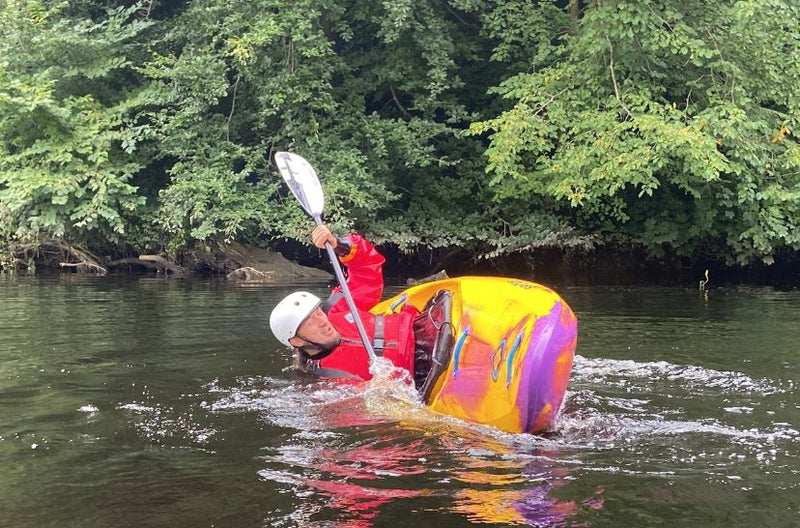 Person in a colorful kayak with a paddle, surrounded by greenery on a river.