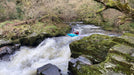 Person kayaking through a rocky river with greenery on either side
