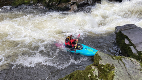 Person kayaking in a river with rapids and rocks