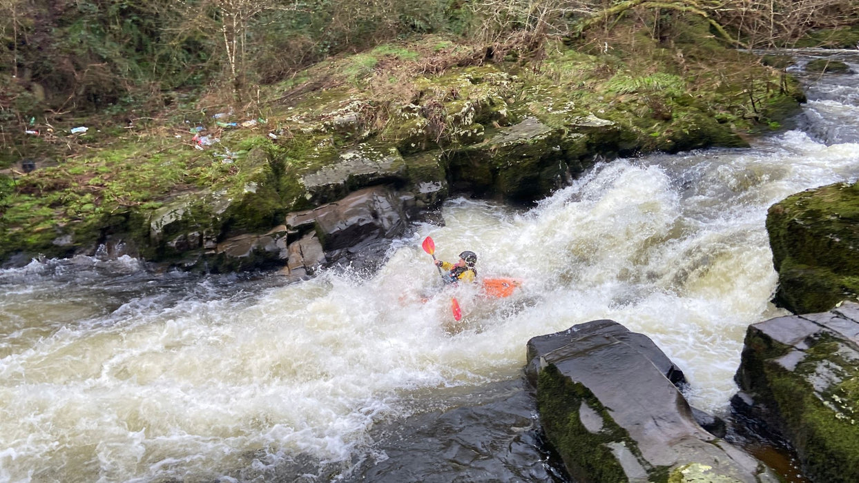 Person kayaking through rapids in a forested area