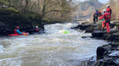 People kayaking and observing rapids in a forested area